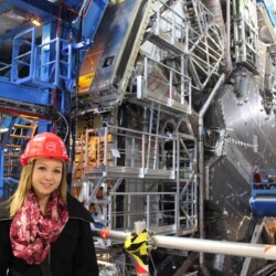 eine Schülerin mit rotem Bauschutzhelm steht in einer Fabrik.