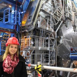 eine Schülerin mit rotem Bauschutzhelm steht in einer Fabrik.